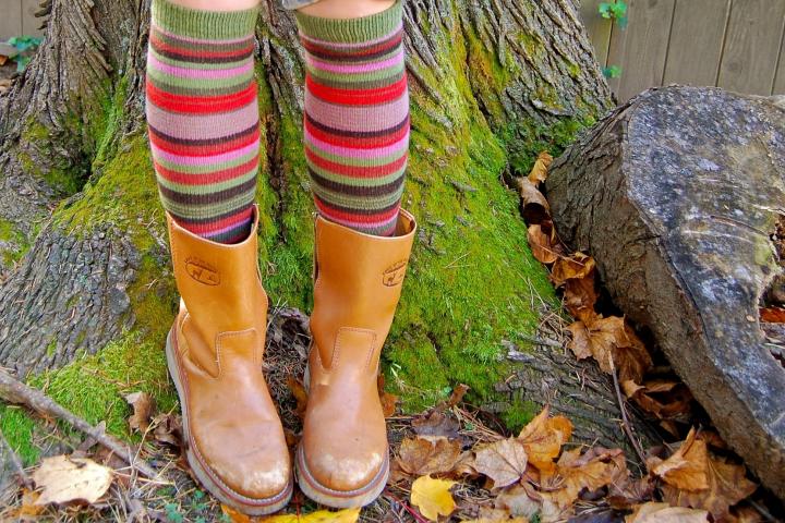 Voeten van een kind met laarzen en hoge gestreepte sokken staan op de voet van een boom in de herfst.